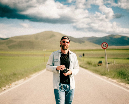 Stefano Vensi sorridente in campagna toscana con macchina fotografica in mano