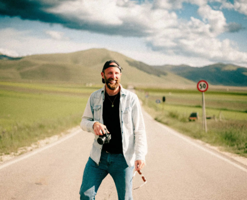 Stefano Vensi vestito informale, sorridente, con macchina fotografica – Toscana